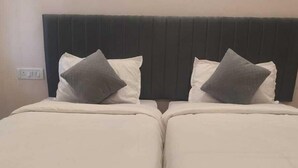 Een tweepersoonsbed met een donker hoofdeinde, twee kussens en een effen muur met een stopcontact.