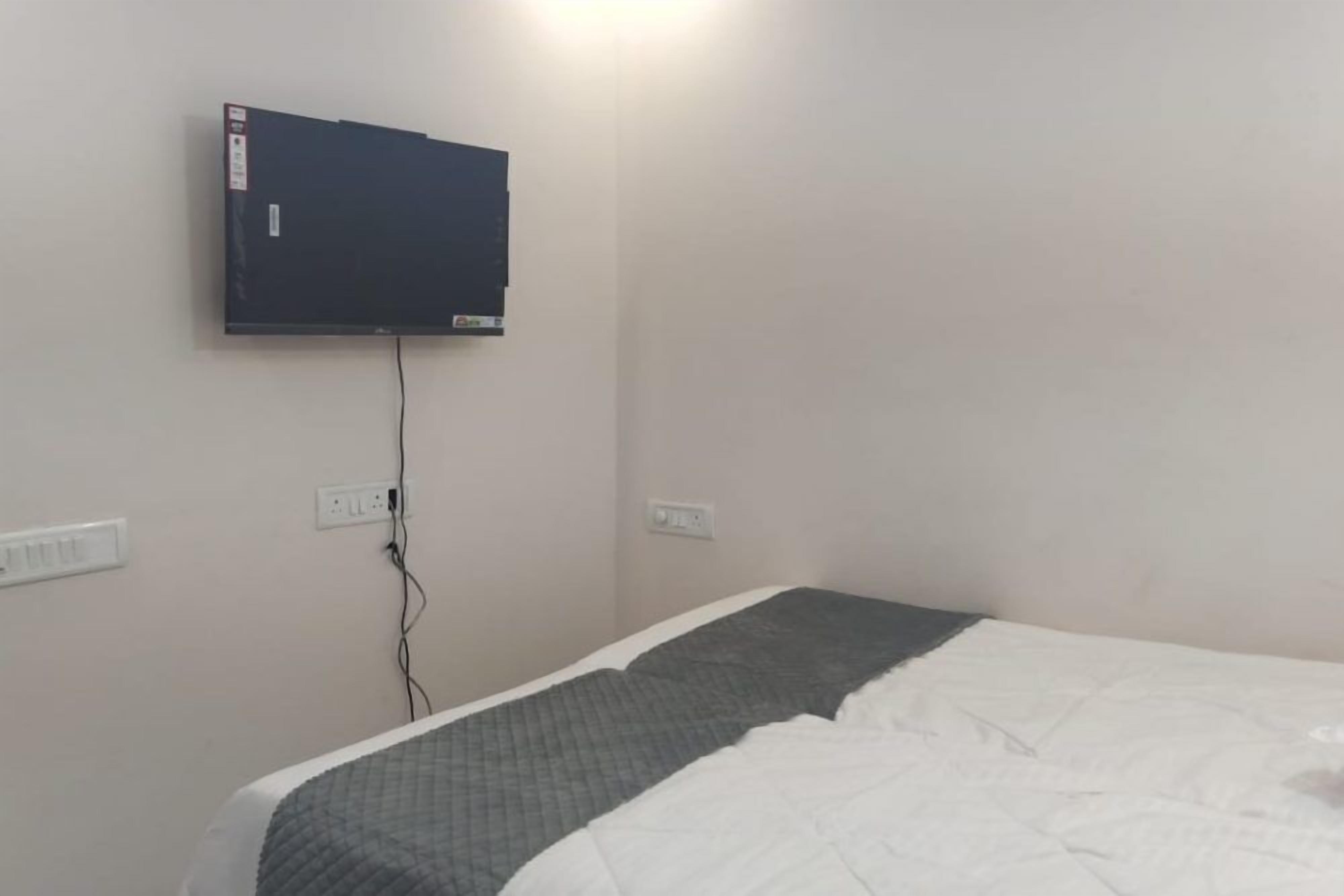 A room with a bed, a flat-screen TV mounted on the wall, and a power outlet.