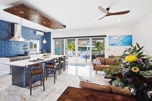 A modern kitchen with a central island, bar stools, and a dining area with a sofa and coffee table. -     Luxury Canalfront Villa | 3BR | Private Pool/Hot Tub | 5 Min to Grace Bay (Leeward)