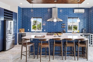 A modern kitchen with blue tiled walls, stainless steel appliances, and a central island with bar stools. -     Luxury Canalfront Villa | 3BR | Private Pool/Hot Tub | 5 Min to Grace Bay (Leeward)