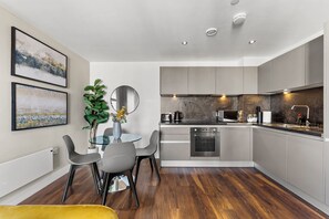 Una cocina moderna con gabinetes grises, un horno empotrado y un comedor con mesa de vidrio y sillas grises.