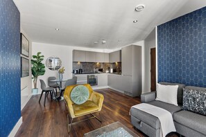 Una cocina moderna con electrodomésticos integrados, un comedor con una silla amarilla y una sala de estar con un sofá gris.
