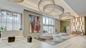 Eine großzügige Lobby mit modernem Design, inklusive eines großen abstrakten Gemäldes, einer runden Sitzecke und einem Empfangsbereich.