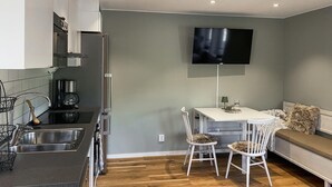 Eine kompakte Küche mit modernen Geräten, ein Essbereich mit Tisch und Stühlen sowie ein an der Wand befestigter Flachbildfernseher.