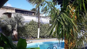 A pool area with a tiled pool, surrounded by lush greenery including palm trees and other tropical plants. - Beach house in Porto de Galinhas with private pool. (Ipojuca)