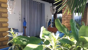 A room with a brick wall, a blue chair, a wooden desk, and a curtain. - Beach house in Porto de Galinhas with private pool. (Ipojuca)