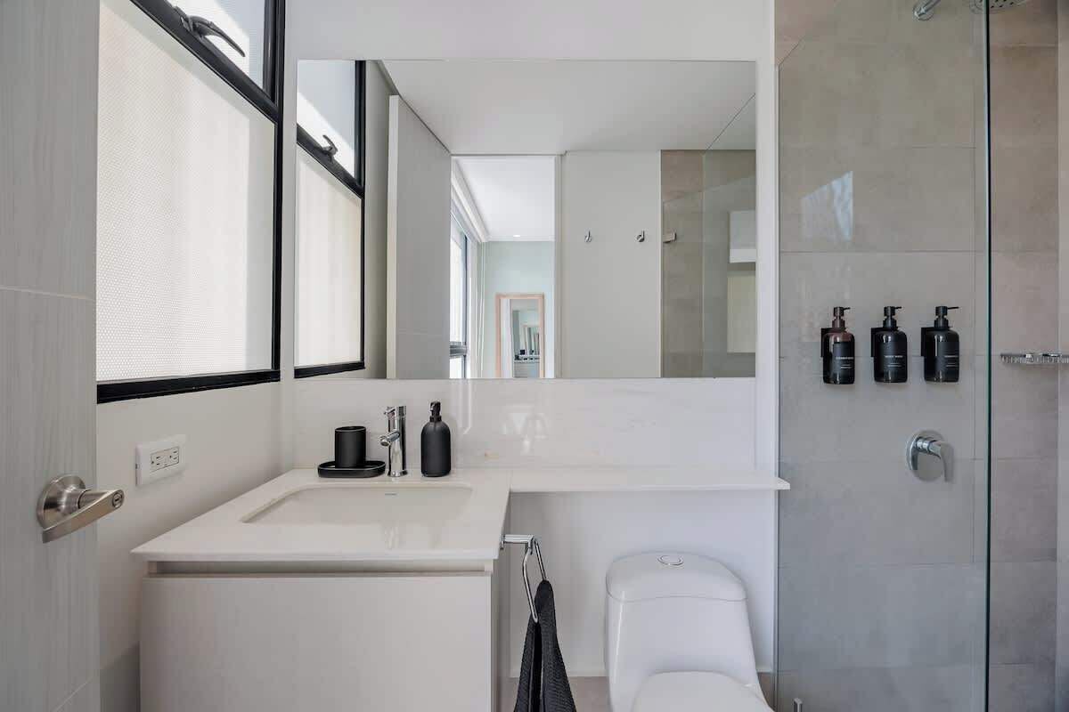 Un bagno moderno con uno specchio grande, un lavandino bianco e un box doccia in vetro.