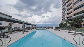 A swimming pool with a covered area, surrounded by buildings and mountains in the background. - lEPl Nice Apt w/Pool, Good Zone, Bbq & Balcony (Medellín)