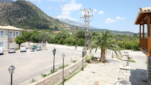 A street view with a building, parked cars, a palm tree, and mountains in the background. - Despotato (Sparta)