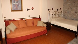 A room with a red sofa, a single bed, a painting of a ballerina, and a stone wall. - Despotato (Sparta)