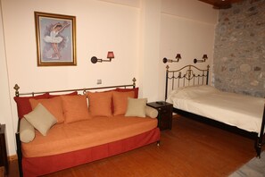 Una habitación con un sofá rojo, una cama individual, un cuadro de una bailarina y una pared de piedra.