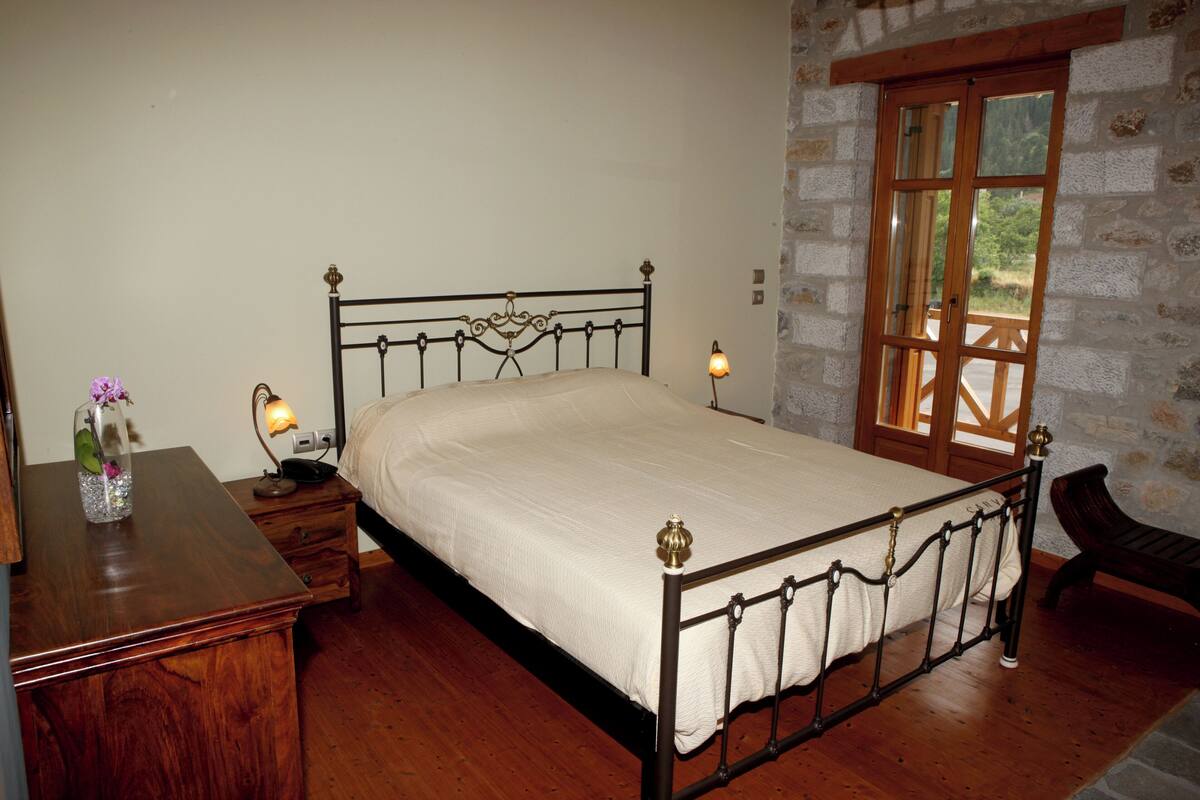 Un dormitorio con una cama de madera, mesitas de noche, una lámpara y una pared de piedra con una ventana.