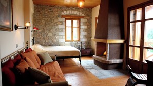 Une chambre avec un mur en pierre, un lit, un banc et une cheminée.