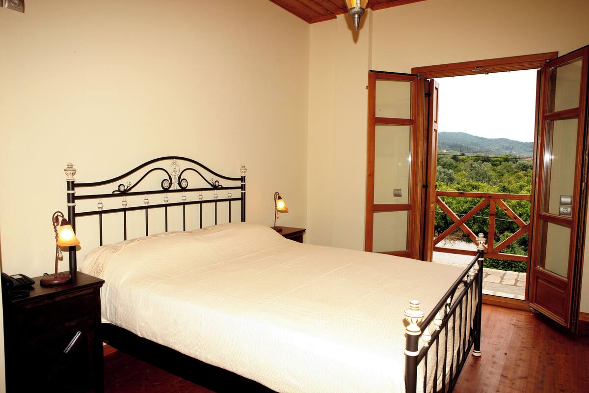 Un dormitorio con cama, lámparas de noche y vistas a un balcón exterior desde una puerta abierta.