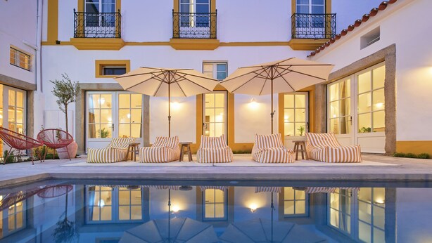A poolside area with lounge chairs and umbrellas, reflecting the building's windows. - Pátio do Tempo (Évora)