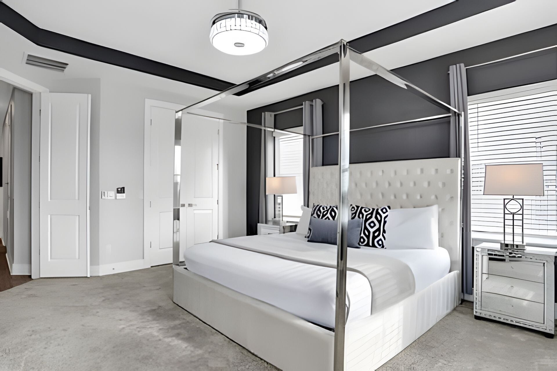 A modern bedroom with a four-poster bed, a nightstand, and a window with blinds.