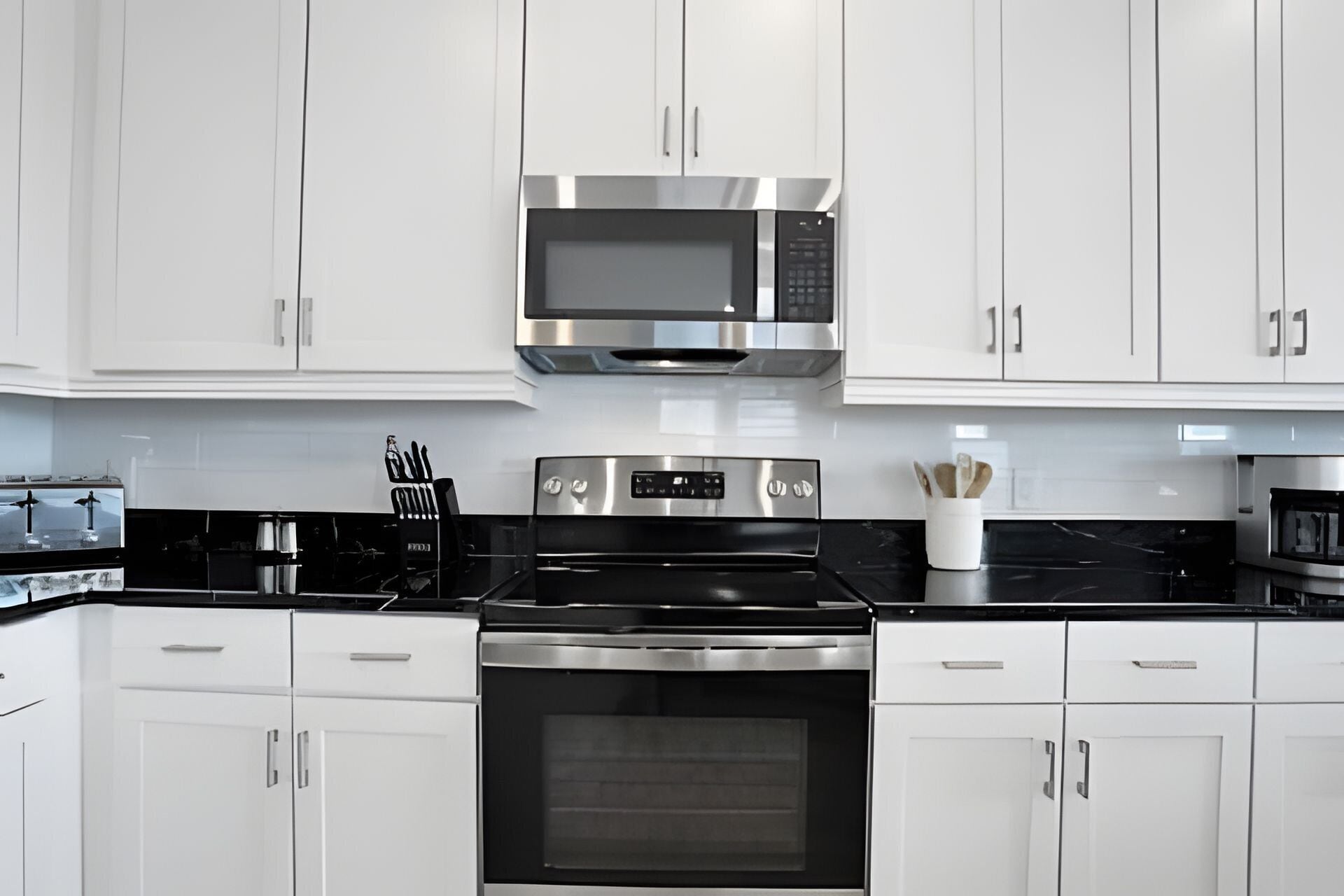 A modern kitchen with white cabinets, stainless steel appliances including a microwave, oven, and stove, and a black countertop.