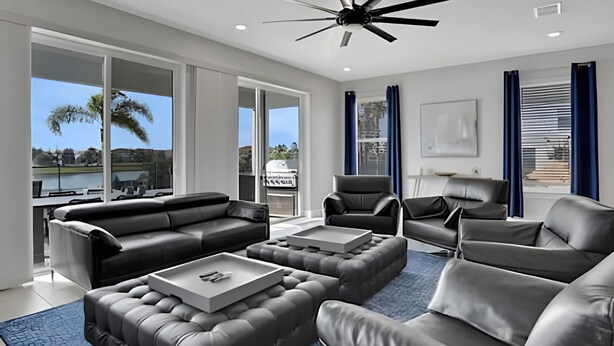 A modern living room with leather sofas, a coffee table, and a ceiling fan. Large windows offer a view of the outdoors. - Reunion Luxury Villa w/ Lake View & Game Room (Kissimmee)