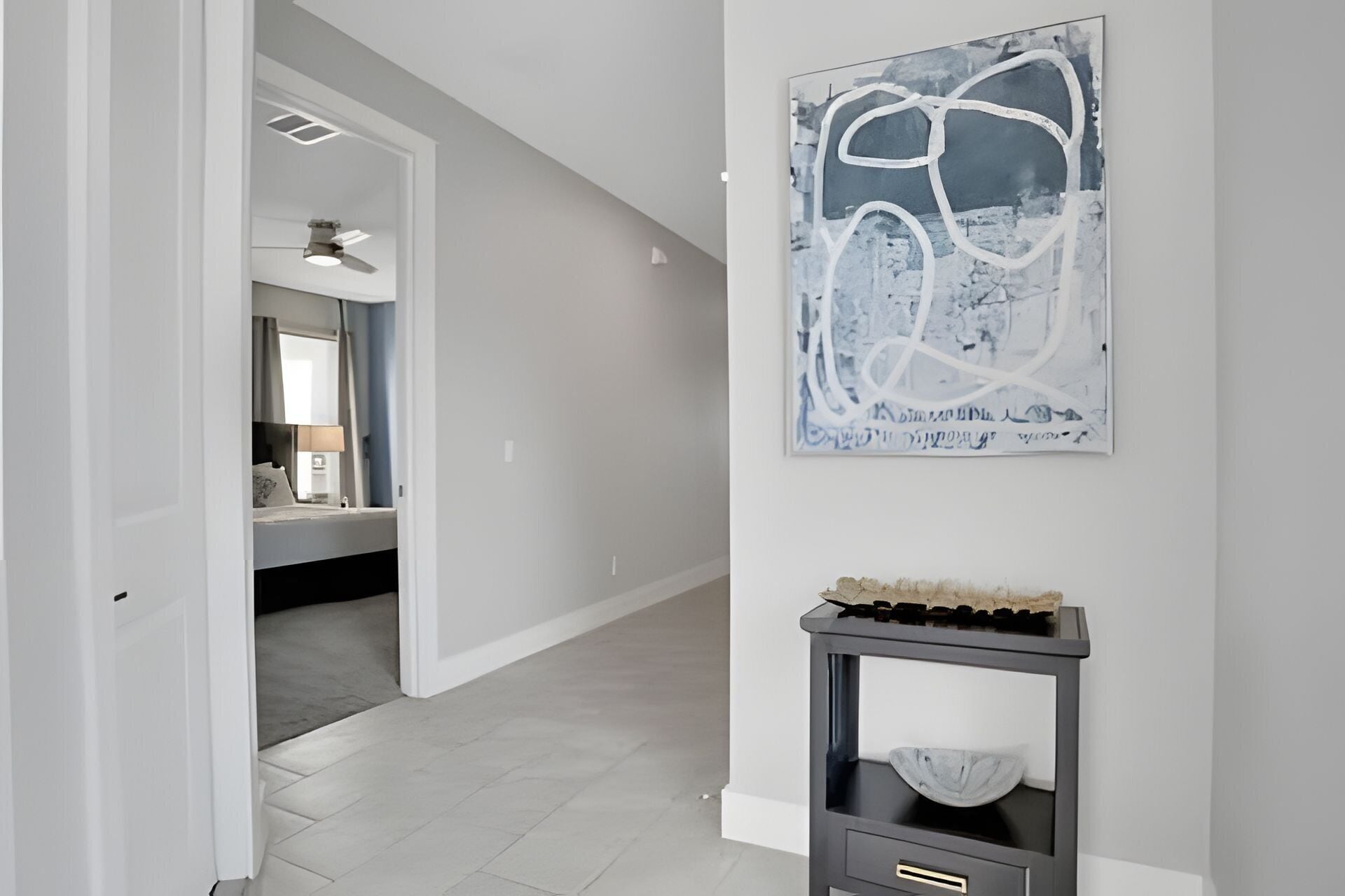 A hallway with a modern abstract painting, a dark console table with a bowl, and a room visible through an open door.