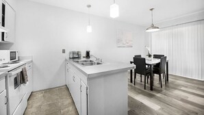 Una cocina moderna con armarios blancos, una isla central con un lavamanos y un comedor con mesa y sillas.