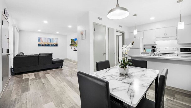 Una cocina moderna con gabinetes blancos, un comedor con una mesa de mármol y un sofá gris en un luminoso salón minimalista.