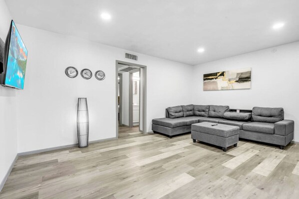 A modern living room with a sectional sofa, a coffee table, and a flat-screen TV mounted on the wall.