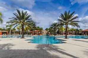 A large outdoor swimming pool surrounded by palm trees and lounge chairs, with a waterfall feature in the background. - 5BR Villa w/ Pool + Resort Access – Solterra (Davenport)