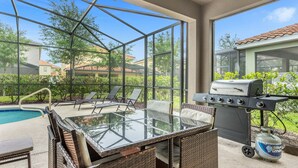 An outdoor patio with a glass table, wicker chairs, a barbecue grill, and a pool. - 5BR Villa w/ Pool + Resort Access – Solterra (Davenport)