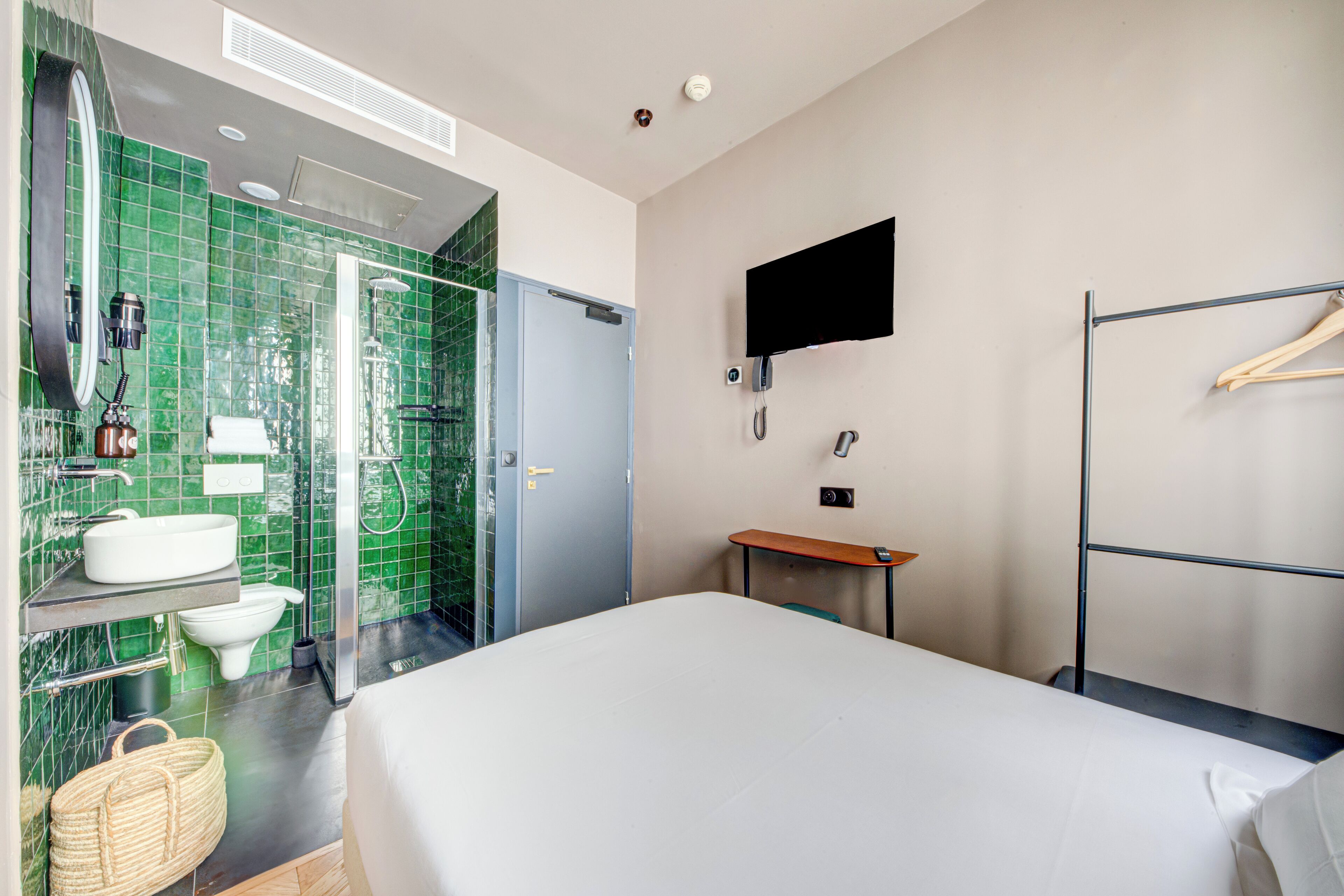 A hotel room with a bed, a bathroom with a shower, a sink, and a television mounted on the wall.