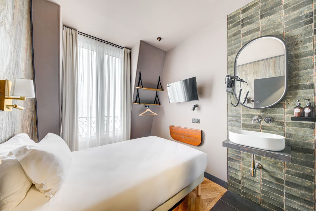 A hotel room with a bed, a large mirror, a wall-mounted TV, and a bathroom with a sink and mirror.