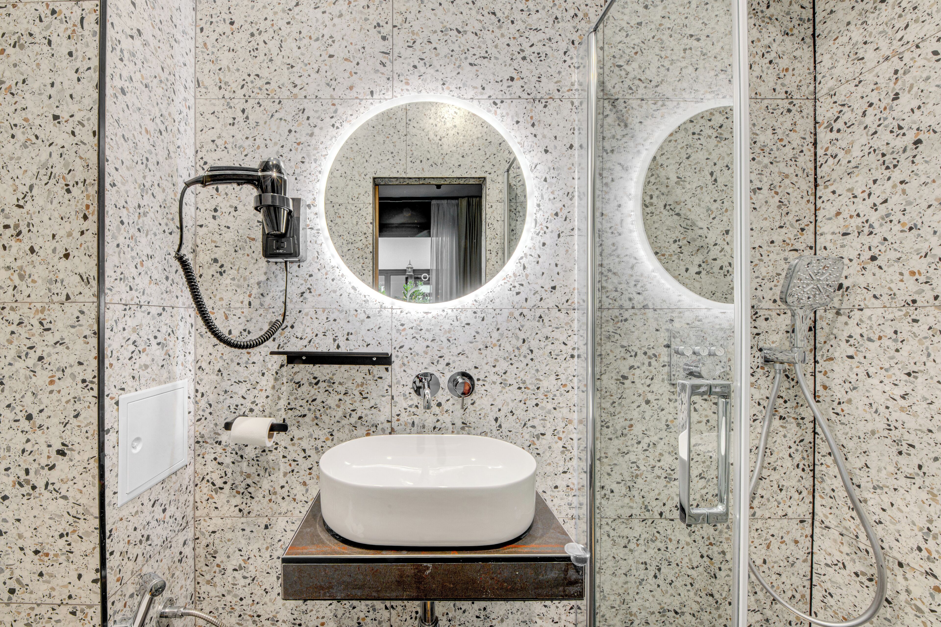 A modern bathroom with a freestanding sink, a handheld showerhead, and a wall-mounted mirror.
