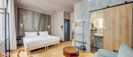 Una habitación de hotel moderna con una cama grande, una mesa de madera, un sofá y un baño con espejo y lavabo.