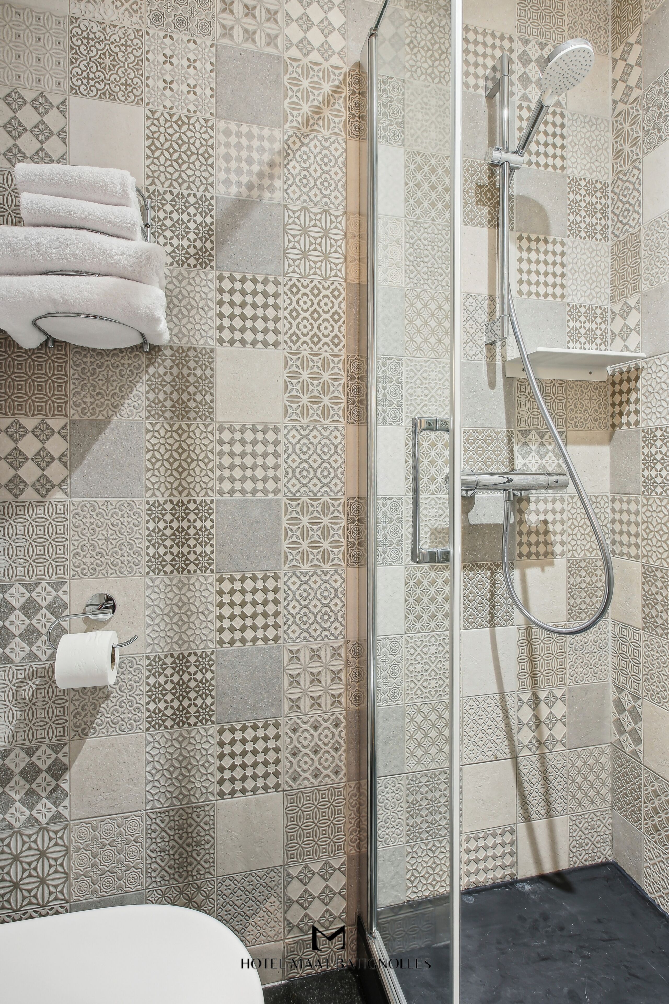 Une salle de bain avec des carreaux décorés, une douche en verre et des toilettes avec un rouleau de papier toilette.