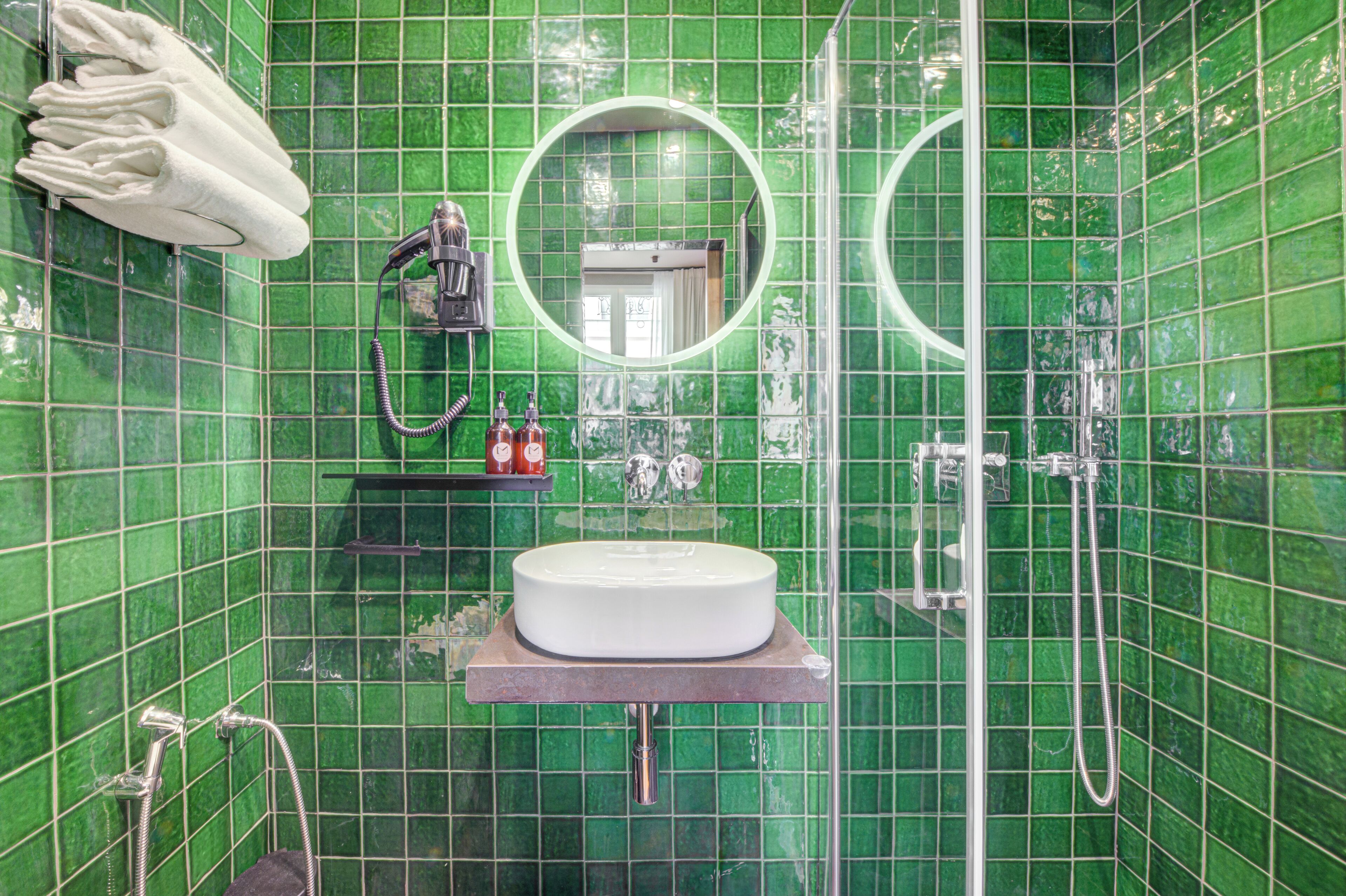 A bathroom with green tiles, a round mirror, a sink, and a towel rack.