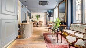A spacious living area with a wooden floor, a large window, a seating area with a patterned rug, and a stone wall in the background. - Hôtel Maât Batignolles (Paris)