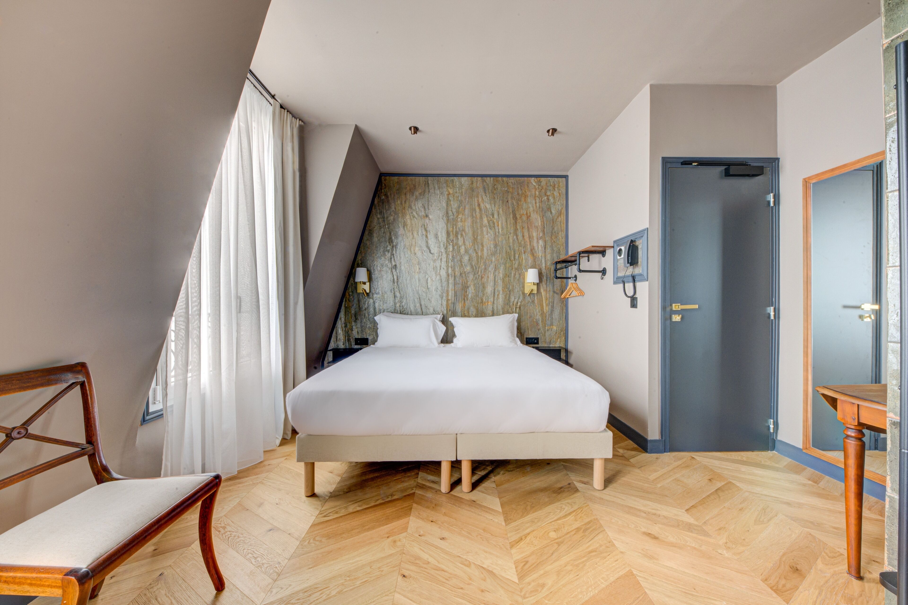 A bedroom with a bed, a chair, a desk, a door, and a window with curtains.