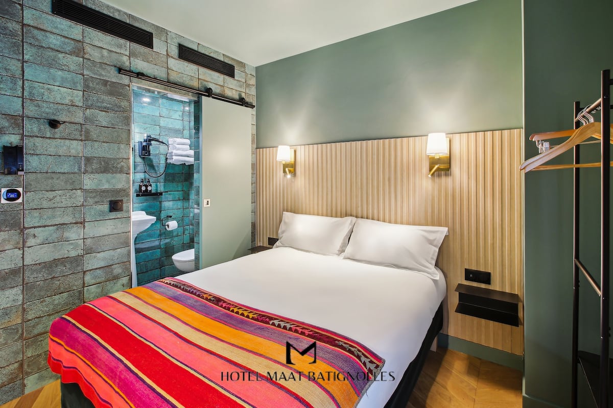 A hotel room with a bed, a shower, a wooden headboard, and a striped blanket.
