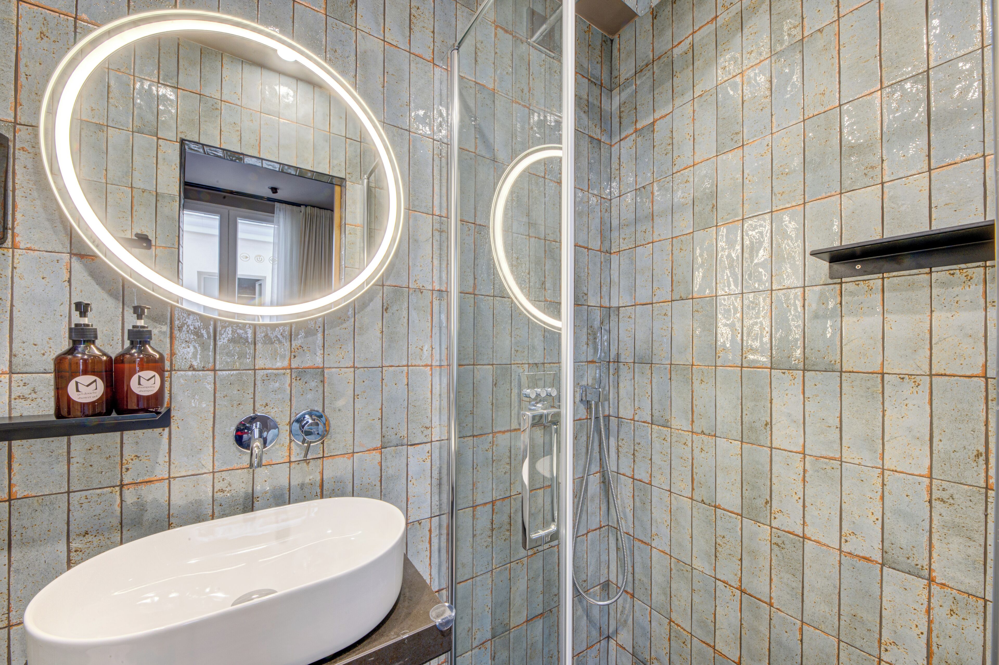 Ein Badezimmer mit einem weißen Waschbecken, zwei Seifenspender, einem Spiegel mit Beleuchtung und einer Duschkabine.