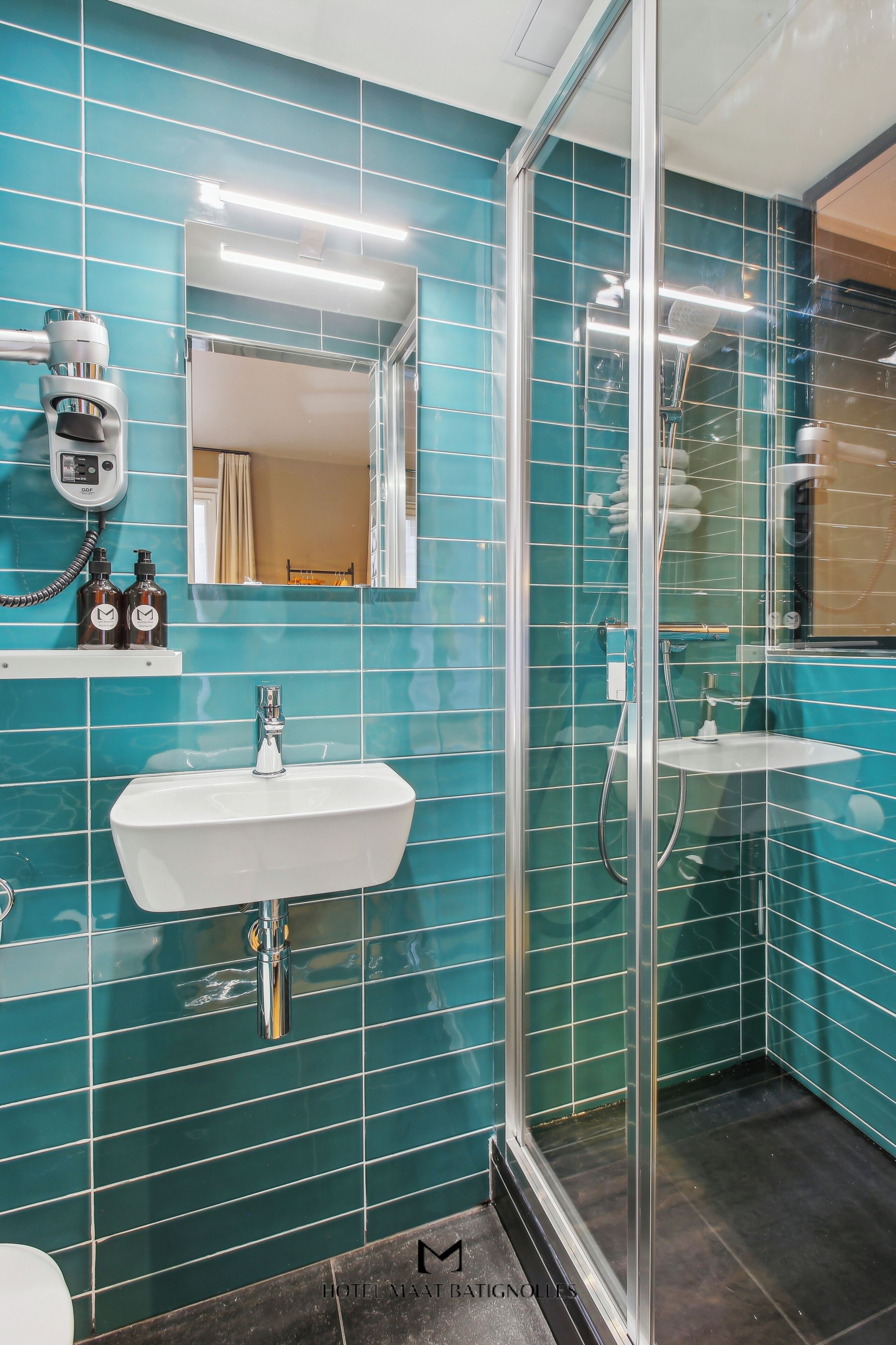 Un baño con azulejos color turquesa, una ducha con cerramiento de vidrio, un lavamanos blanco y un espejo sobre el lavamanos.
