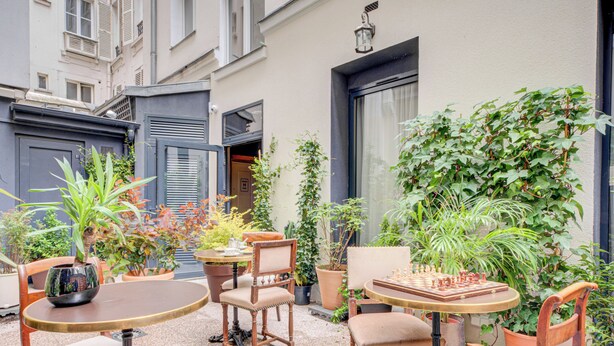 An outdoor patio with wooden furniture, potted plants, and a chessboard. - Hôtel Maât Batignolles (Paris)