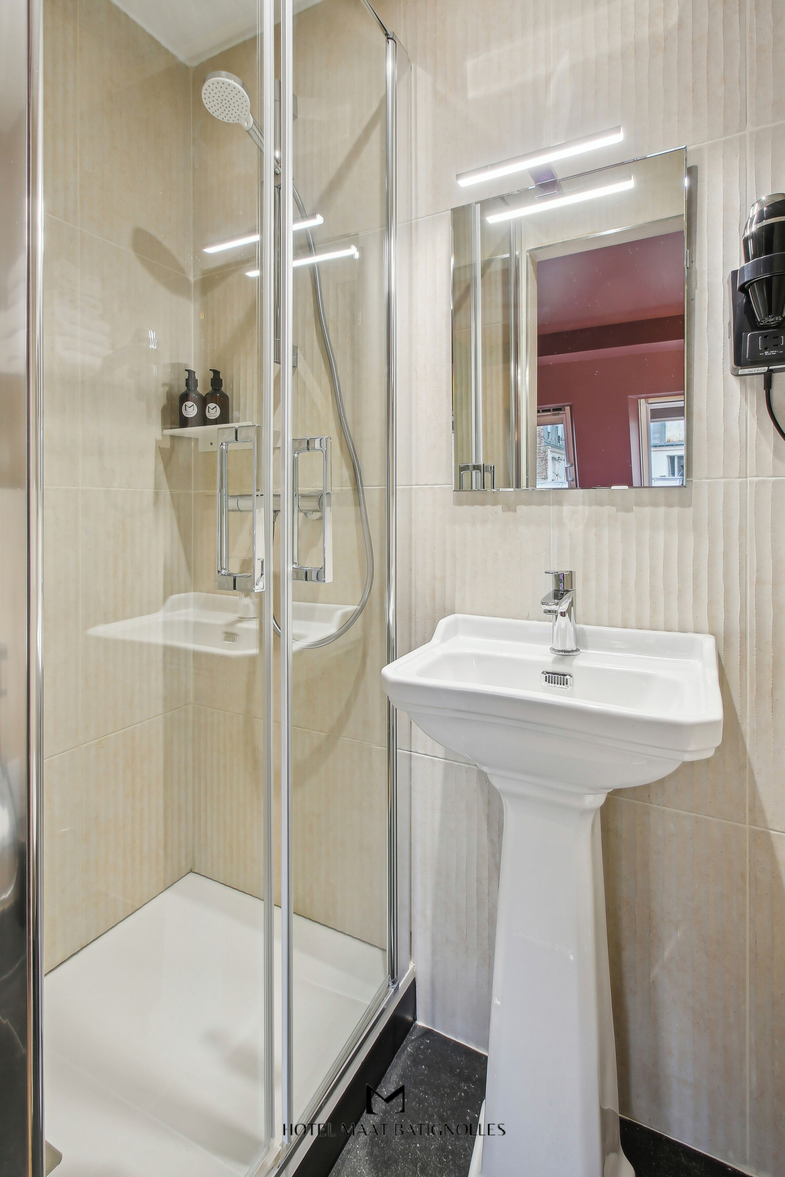 Un baño moderno con ducha de vidrio, lavamanos sobre pedestal y espejo por encima.