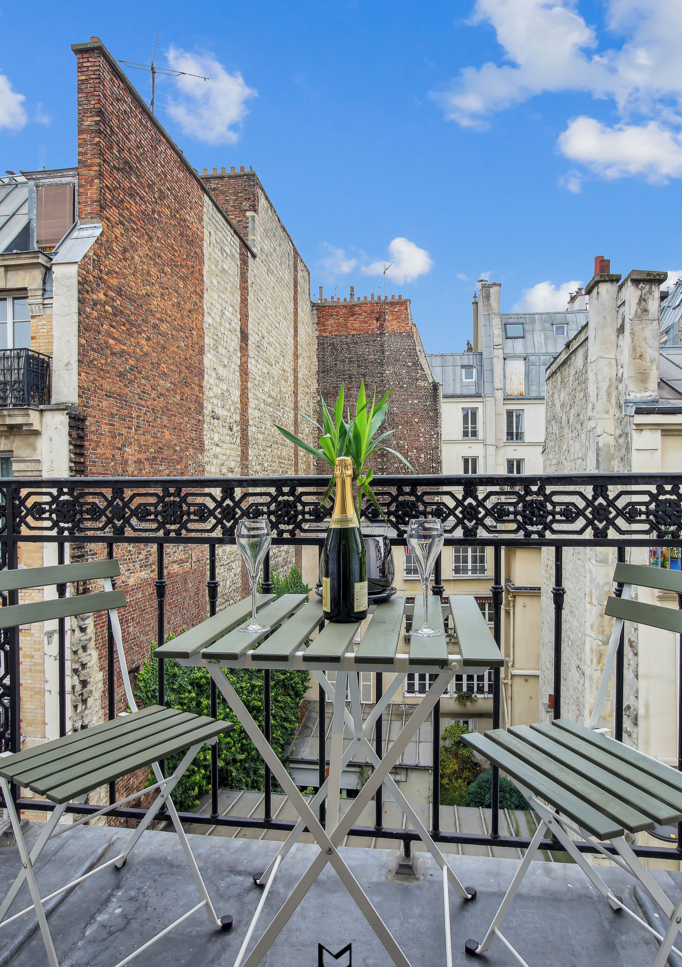 A rooftop terrace with a table, chairs, and a bottle of champagne.