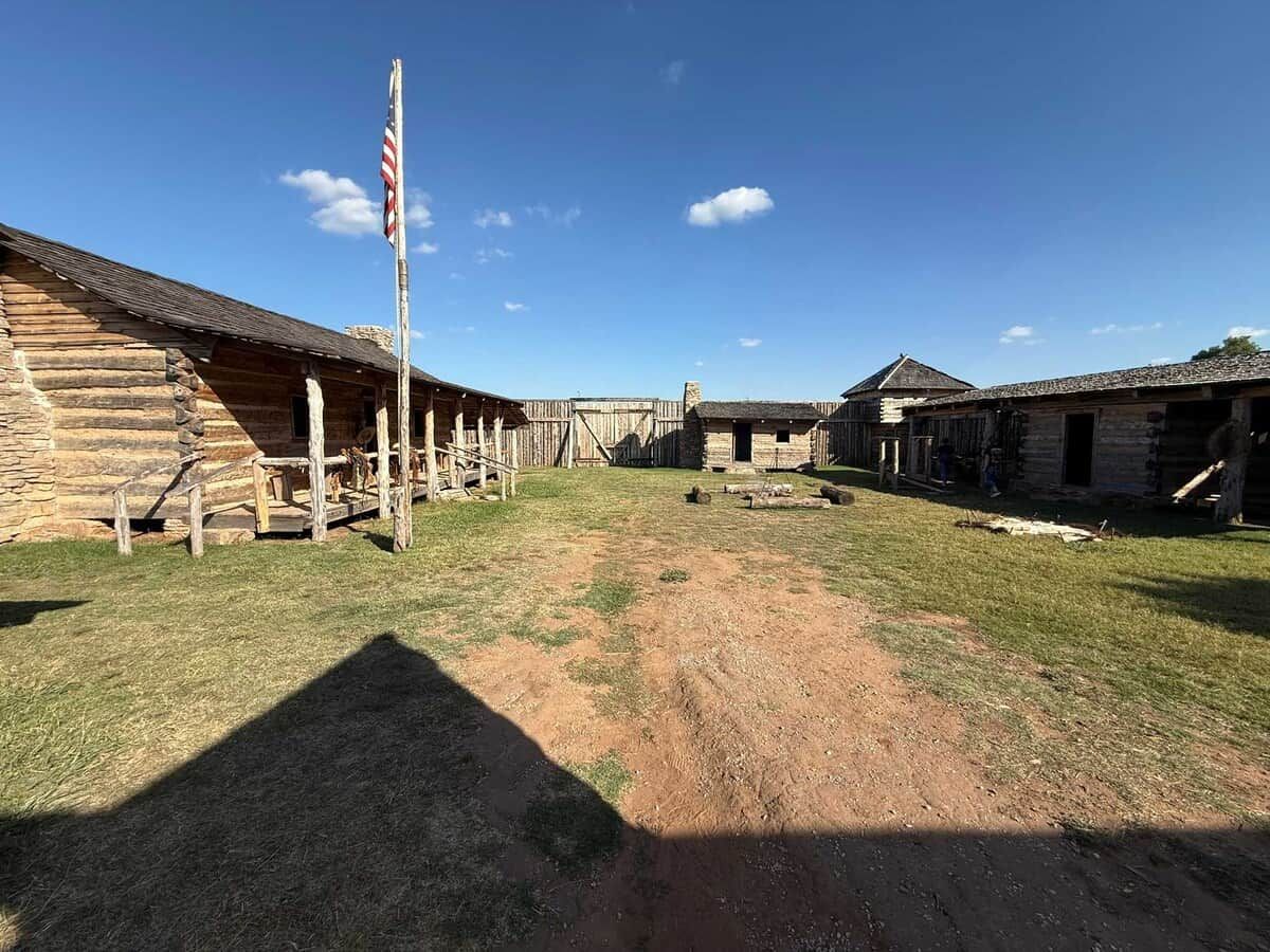 A rustic log cabin with a porch, a flagpole, and a clear sky.