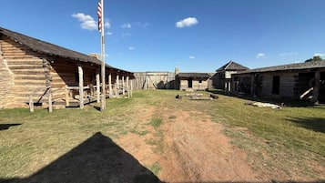 A rustic log cabin with a porch, a flagpole, and a clear sky.