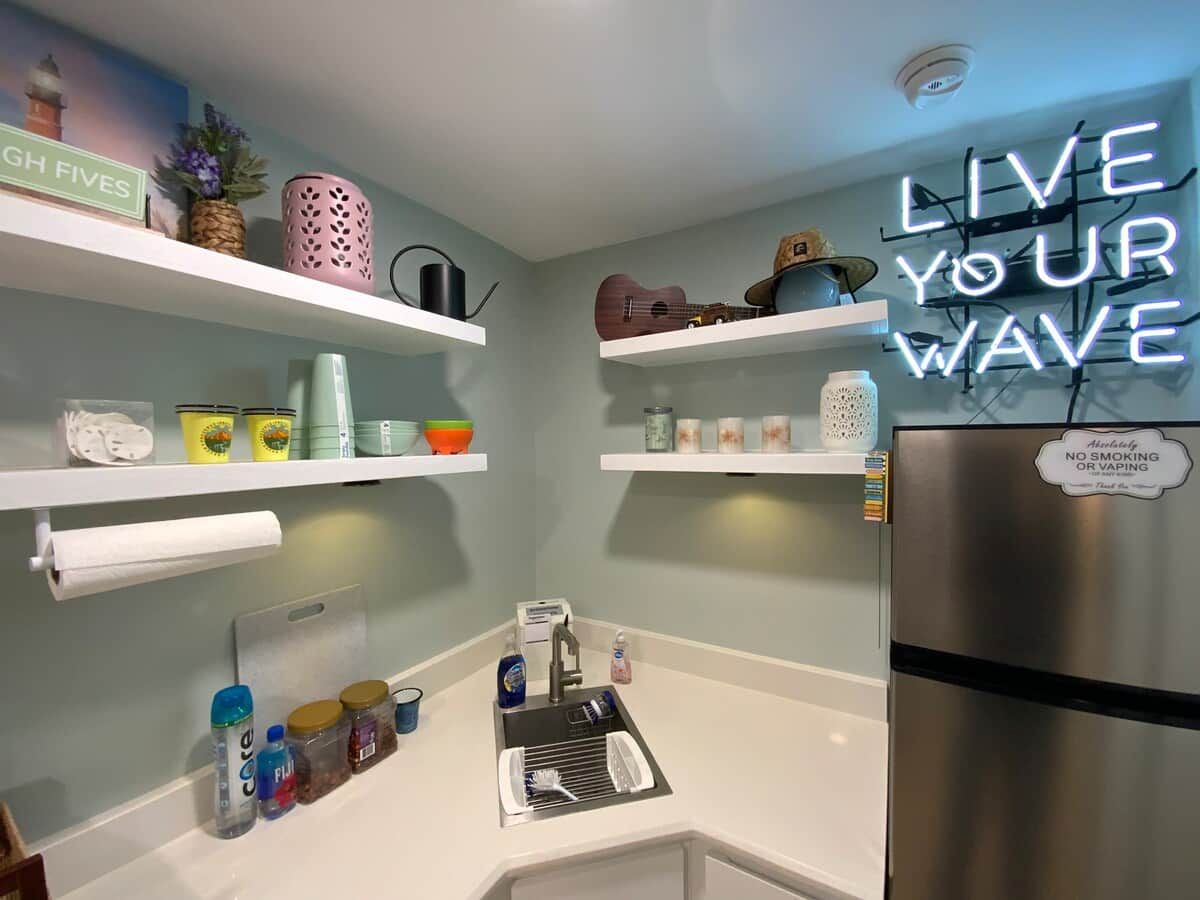 A kitchen with white countertops, a stainless steel refrigerator, and various kitchen items on shelves.