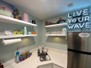 A kitchen with white countertops, a stainless steel refrigerator, and various kitchen items on shelves.