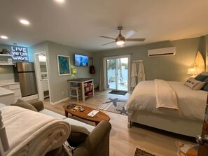 Una habitación de hotel con cama, escritorio, silla, televisor y ventilador de techo.