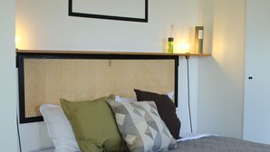A neatly made bed with a grey bedspread and multiple pillows, a woven headboard, and a framed picture above the bed. - Lodges Mont-Vert (Le Robert)