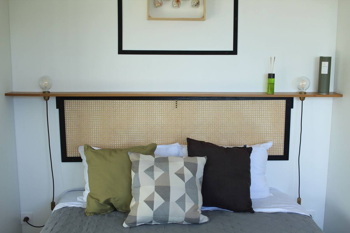 A neatly arranged bed with a headboard, pillows, and a shelf with decorative items.