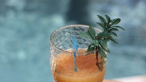 A cocktail glass with a sprig of rosemary on a wooden coaster by a pool. - Lodges Mont-Vert (Le Robert)